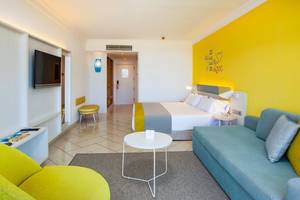 Innenansicht eines Zimmers im Abora Catarina Hotel mit gelber Wand, Doppelbett, Sofa und Tisch.