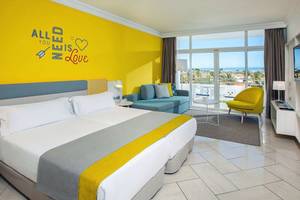 Hotelzimmer im Abora Catarina by Lopesan Hotels mit gelber Wand, zwei Betten, Sofa und Blick auf den Ozean.