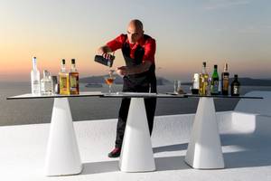 Ein Barkeeper bereitet einen Cocktail auf einer weißen Tischplatte bei Sonnenuntergang zu.