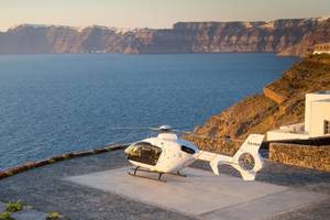 Ein weißer Hubschrauber parkt auf dem Gelände des Ambassador Aegean Luxury Hotel & Suites mit Blick auf das Meer und die Berge.