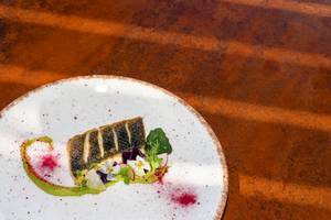 Gebratener Fisch auf einem weißen Teller mit grünem Gemüse und Blumen.
