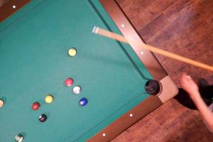 Ein Blick von oben auf einen Pooltisch mit bunten Kugeln und einem Stock.