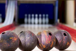 Vier Bowlingkugeln auf einer Bowlingbahn mit Bowlingkegeln im Hintergrund.