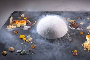 Ein Dessert auf einem schwarzen Teller im Elysium Resort & Spa, umgeben von Rauch und verschiedenen Süßigkeiten.