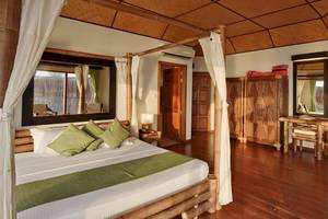 Schlafzimmer im Safari Island Resort mit Himmelbett, grünen Kissen und Holzboden.