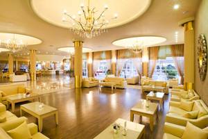 Lobby des Kipriotis Village Resorts mit goldenen Kronleuchtern und cremefarbenen Sofas.