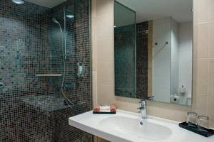 Badezimmer im Riu Lupita Hotel mit gefliester Wand, Dusche, Waschbecken und Spiegel.