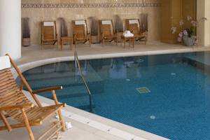 Innenpool des Aquila Porto Rethymno Hotels mit Holzstühlen und Handläufen.