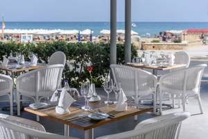 Außensitzbereich des Aquila Porto Rethymno Hotels mit weißen Tischen und Stühlen am Meer.