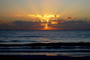 Sonnenuntergang am Strand mit Meer und Wolken, goldene Sonne hinter den Wolken.