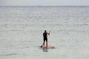 Ein Mann steht auf einem roten Surfbrett und paddelt auf dem offenen Meer.