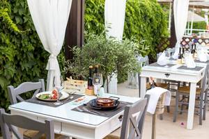 Hotelterrasse mit Tisch, Speisen und Getränken, umgeben von Pflanzen.