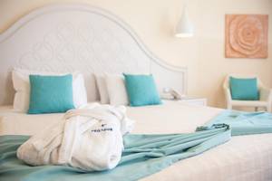 Doppelbett im Pegasos Deluxe Beach Hotel mit türkisfarbenen Kissen und einem weißen Bademantel.