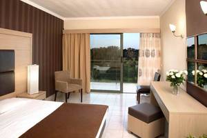 Innenansicht eines Hotelzimmers im Kipriotis Hippocrates Hotel mit Bett, Sesseln, Schreibtisch und Terrassentür.
