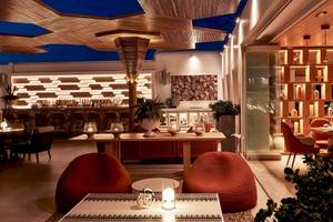 Inneneinrichtung des Myconian Naia Hotels mit Bar, Esstischen und roten Sesseln.