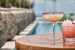Zwei Cocktails auf einem runden Tisch neben einem Pool im Myconian Naia Hotel.