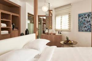 Schlafzimmer im Myconian Naia Hotel mit weißem Bett, weißem Kopfteil, Nachttisch, Fernseher an der Wand und Badezimmer im Hintergrund.