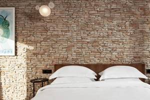 Schlafzimmer im Myconian Naia Hotel mit Steinwand und weißen Bettlaken.