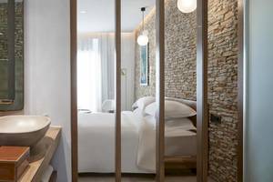 Schlafzimmer im Myconian Naia Hotel mit einem Bett, Kissen, einem Steinwand, einem Waschbecken, Spiegel und Vasen.