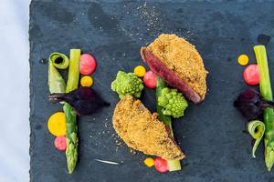 Foto eines Gourmetgerichts von Myconian Naia Hotel mit Steak, Gemüse und Beilagen auf schwarzem Teller.