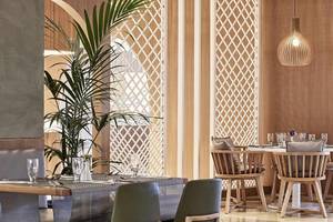 Restaurant-Innenansicht des Atlantica Marmari Palace mit Holzmöbeln, Tisch, Stühlen, Pflanzen und Pendelleuchte.