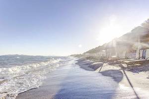 Strandszene mit Sonnenliegen und Sonnenschirmen am Meer, klares Wetter.