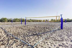 Volleyballfelder auf einem Sandstrand mit blauen Netzen und Pfosten.