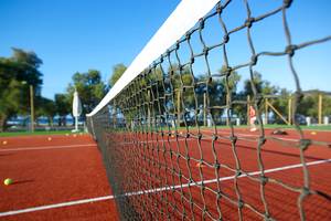 Tennisnetz auf einem roten Platz mit mehreren Tennisbällen im Hintergrund.