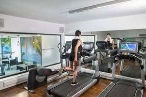 Fitnessraum im Cavo Maris Beach Hotel mit Personen auf Laufbändern und einer reflektierten Umgebung.