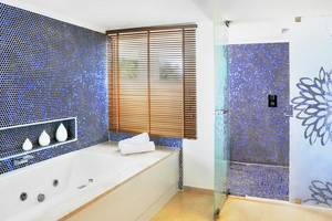 Ein Badezimmer mit blauen Fliesen, Badewanne, Dusche und Fenster mit Jalousien.