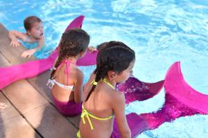 Kinder im Schwimmbad mit Mermaid-Schwänzen, eines schwimmt im Wasser