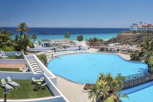 Luftaufnahme des Swimmingpools des Fuerteventura Princess Hotels mit Sonnenliegen und Blick auf das Meer.