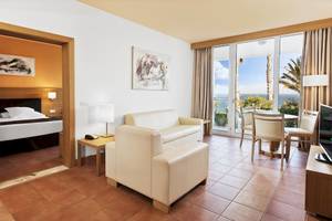 Innenansicht eines Zimmers im Fuerteventura Princess Hotel mit Bett, Wohnzimmerbereich, Esstisch und Meerblick.