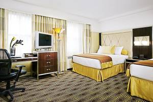 Zimmer im New Yorker Hotel mit zwei Betten, Schreibtisch, Stuhl und Fernseher.