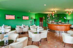 Cocktail-Bar im Occidental Jandia Royal Level Hotel mit grünen Wänden, weißen Stühlen und einer Theke.