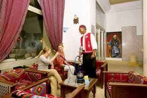 Im Hotel Calimera Yati Beach sitzen zwei Frauen in der Lounge und genießen eine Shisha, während ein Mann ihnen serviert.