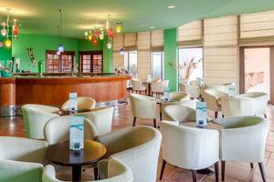 Bar im Occidental Jandia Royal Level Hotel mit grünen Wänden und weißen Stühlen.