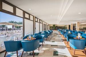Innenbereich des Occidental Jandia Mar Hotels mit vielen blauen Stühlen und Tischen, große Fenster und Sonnenschirme draußen