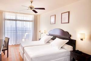 Zwei-Betten-Zimmer im Occidental Jandia Mar Hotel mit weißen Möbeln, Deckenventilator und Fernseher.