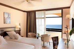 Zweibettzimmer im Occidental Jandia Royal Level mit Meerblick, zwei Betten, Sesseln, Schreibtisch und Aussicht auf das Meer.