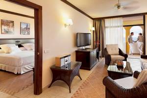 Innenansicht einer Suite im Occidental Jandia Royal Level Hotel mit Schlafzimmer, Wohnzimmer und Balkon.