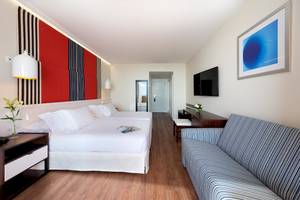Innenansicht eines Zimmers im H10 Tindaya Hotel mit zwei Betten, einer Couch und einer Fernsehwand.