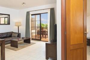 Innenansicht der Suite im Melia Tortuga Beach Hotel mit Wohnzimmer, Couch, Tisch, Lampe, Fernseher und Balkon.