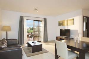 Wohnbereich des Melia Tortuga Beach Hotels mit Couch, Tisch, Fernseher und Balkonzugang