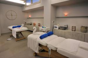 Massageraum im Nelia Beach Hotel & Spa mit zwei Massagetischen, weißen Handtüchern und blauen Kissen.