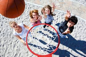 Vier Leute spielen Basketball auf Sand mit einem roten Korb und einem Basketball im Flug.