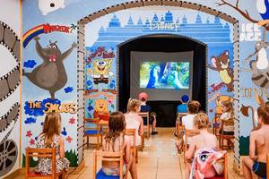 Kinder sitzen in einem Kinobereich im Jaz Lamaya Resort, der mit Disney-Charakteren wie Micky Maus und Winnie Puuh dekoriert ist.