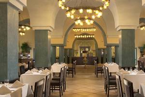 Innenansicht des Restaurants im Jaz Lamaya Resort mit gedeckten Tischen, Kronleuchtern und blauen Säulen.