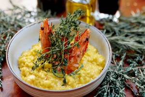Eine Schüssel mit gelbem Risotto, das mit zwei gegrillten Garnelen und frischem Thymian garniert ist.