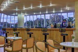 Innenansicht der Bar im Giannoulis Santa Marina Beach Hotel mit runden Tischen, Stühlen und einer Theke mit Getränken.